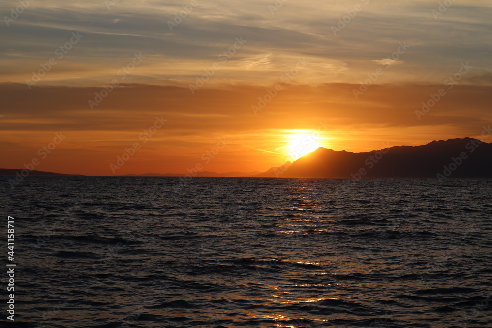 Picturesque orange sunset on the Croatian seaside, Dalmatia, Makarska.  Sunset on the sea, orange sky and silhouette of mountains on the horizon, sun reflection on the water surface