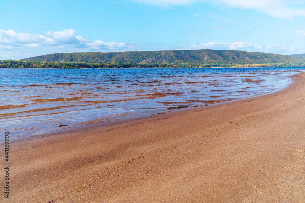 The sandy shore of the big Volga river against the background of blue cloudy sky. On the opposite bank of the Zhiguli Mountains