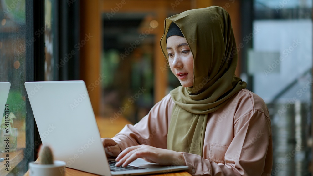 Fototapeta premium Muslim woman wearing hijab working with laptop in coffee shop