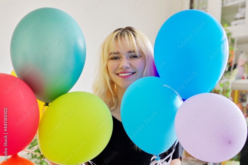 Close up of colored balloons and happy smiling face of blonde teen female