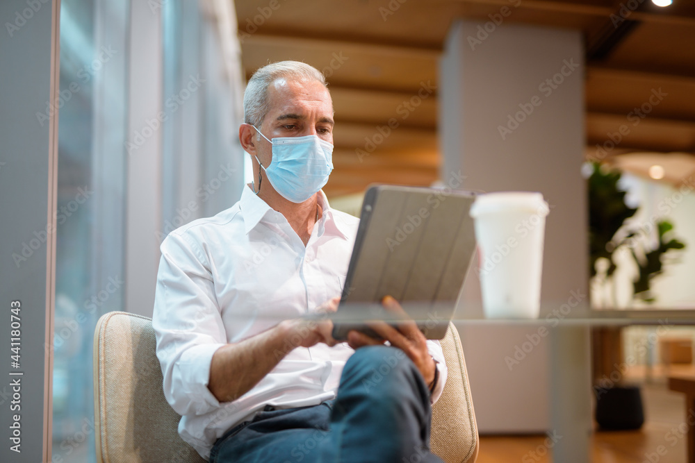Businessman sitting at coffee shop and using digital tablet while wearing face mask and social distancing Businessman sitting at coffee shop and using digital tablet while wearing face mask and social distancing