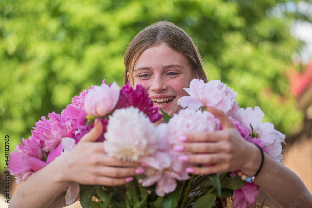 Fototapeta premium Beautiful and happy young girl in the summer with a beautiful bouquet of peonies in nature