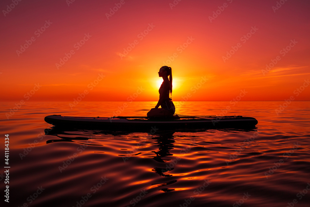 Girl on stand up paddle board at sea with bright sunset or sunrise. Woman relax on sup board in sea.
