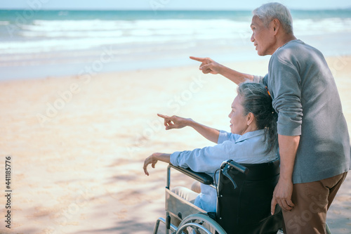 Two elderly couples happily sit in a wheelchair on the beach on their vacation.