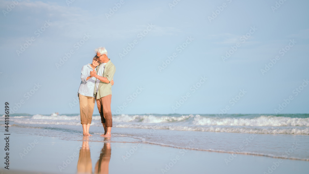 Elderly Asian couple dancing happily on the beach at sunset.