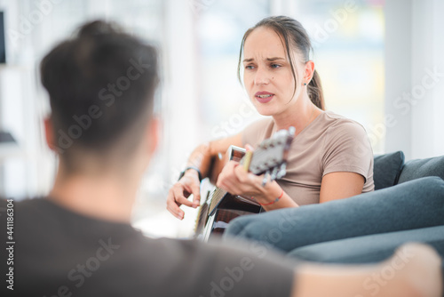 A happy woman playing acoustic guitar and singing on sofa at home, attractive female having fun at home, enjoying melody, musician concept.