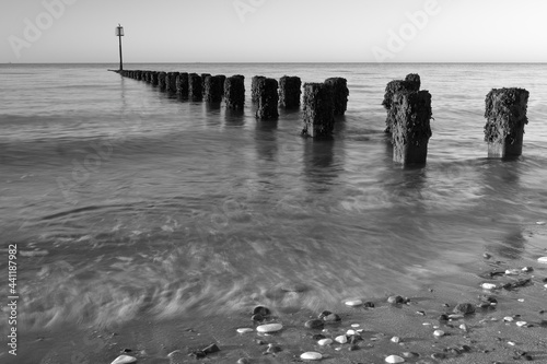 Black and white photograph of groynes at the north beach in Bridlington at dawn  with motion blur of the waves.