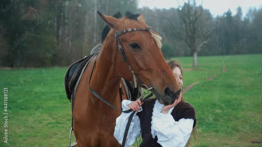 Beautiful young female in a medieval dress stands in a field next to a horse, snow and rain, 4k slow motion. Beautiful young female in a medieval dress stands in a field next to a horse, snow and rain, 4k slow motion.