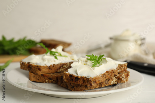 Bread with cream cheese and arugula on white wooden table