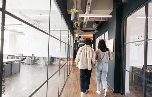 Rear view of young couple walking to office along walkway in open plan building