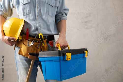 Man worker holding construction helmet and toolbox near wall. Male hand and construction tools