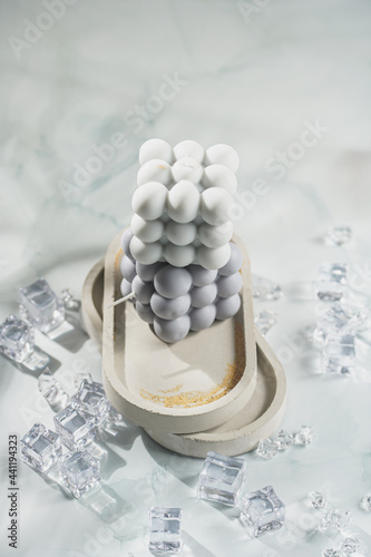 Two grey-blue and white bubble candles on a concrete tray on pastel background stacked on top of each other