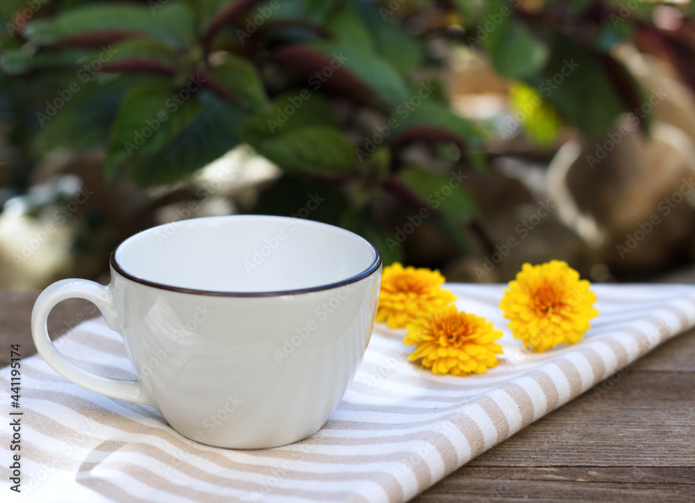 Cozy autumn morning breakfast in the garden. A steaming cup of hot coffee, tea and tagetes flowers in the background on a striped tablecloth. Fall, Thanksgiving concept. Cozy autumn morning breakfast in the garden. A steaming cup of hot coffee, tea and tagetes flowers in the background on a striped tablecloth. Fall, Thanksgiving concept.