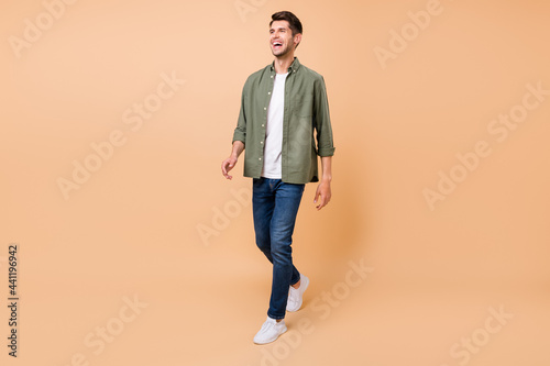 Photo of funny handsome young gentleman wear khaki shirt walking laughing smiling isolated beige color background