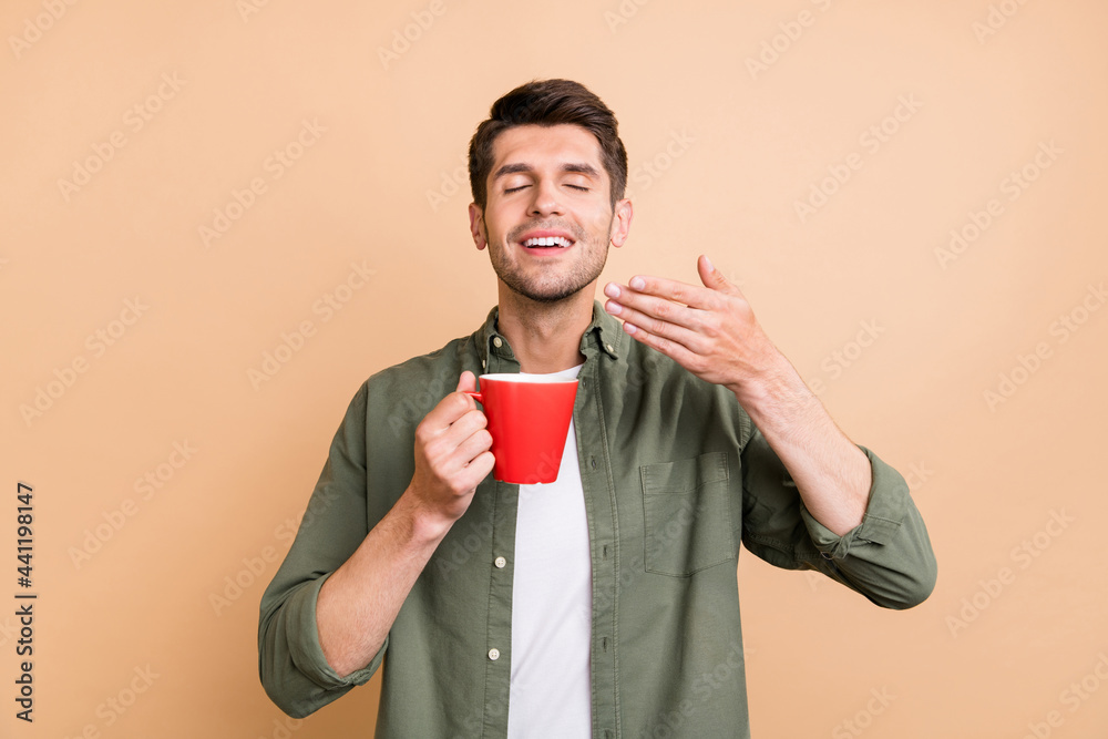 Photo of charming happy cheerful young man smell tea aroma good mood isolated on beige color background Photo of charming happy cheerful young man smell tea aroma good mood isolated on beige color background