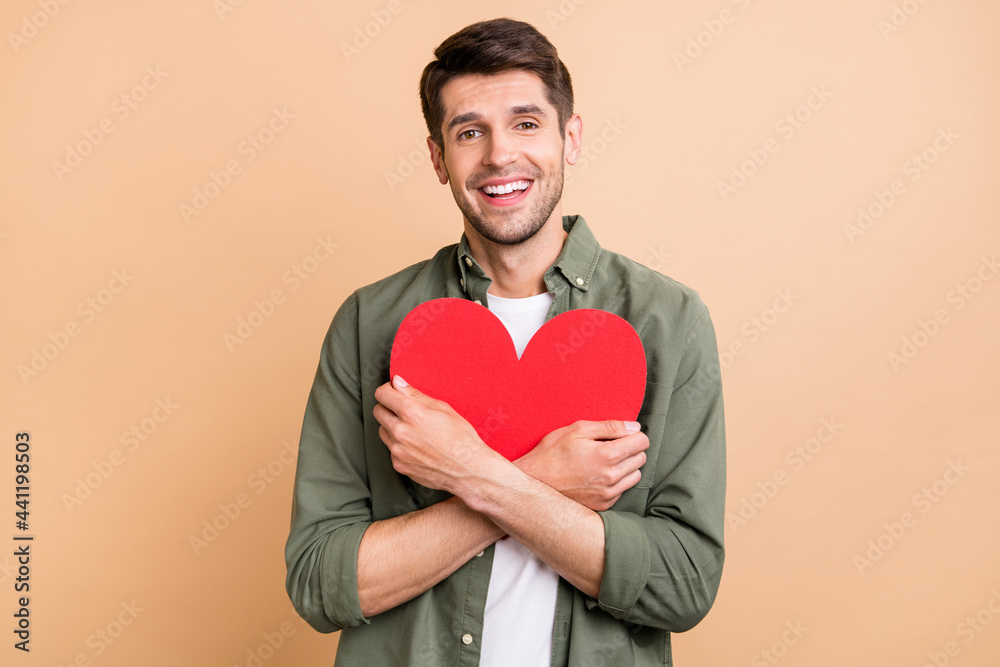 Photo of happy cheerful young man hold hand hug red paper heart smile isolated on pastel beige color background Photo of happy cheerful young man hold hand hug red paper heart smile isolated on pastel beige color background