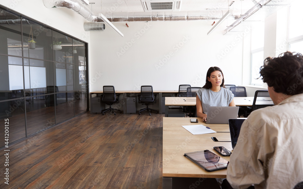 Young couple with laptops at desks working on start up business in rented open plan office space Young couple with laptops at desks working on start up business in rented open plan office space