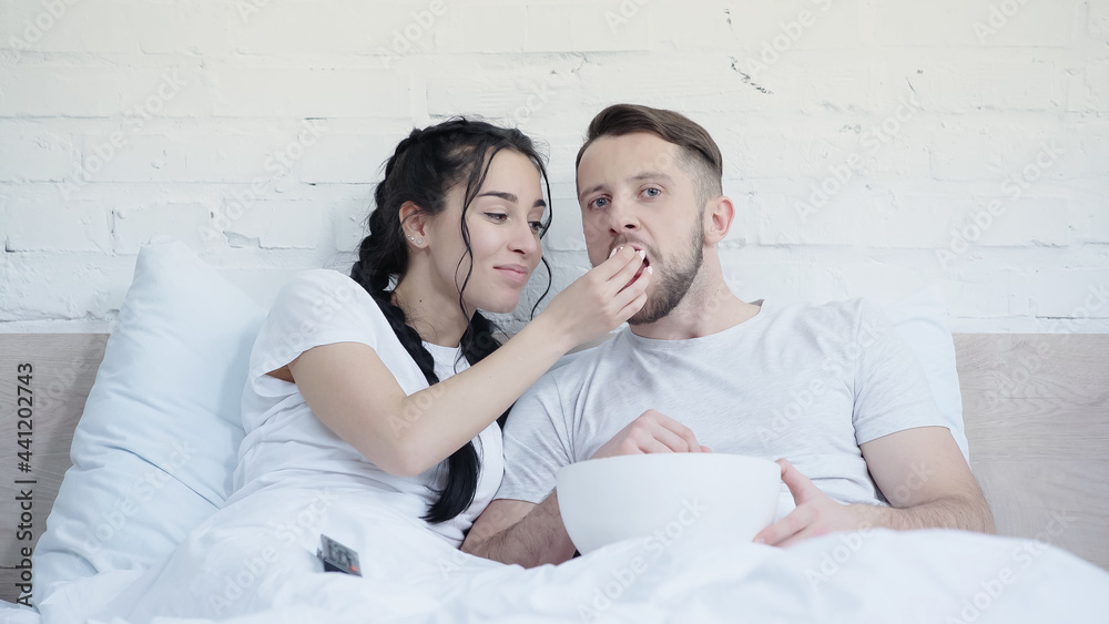 happy young couple eating popcorn and watching movie in bed. happy young couple eating popcorn and watching movie in bed.