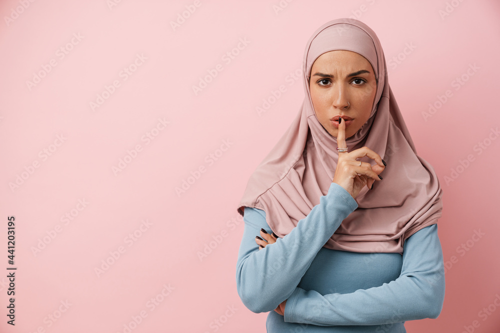 An upset muslim woman wearing pink hijab showing a silence gesture An upset muslim woman wearing pink hijab showing a silence gesture