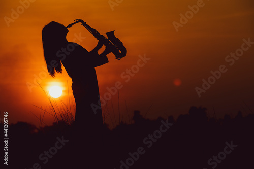 Silhouette of musician with saxophone sunset field,Saxophonist. woman playing on saxophone against the background of sunset