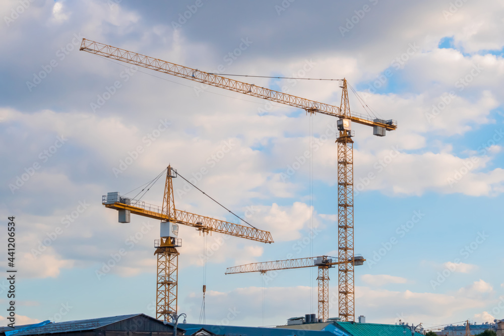 Three yellow tower construction cranes against summer cloudy blue sky. Building process, architecture, urban, engineering, industrial and development concept