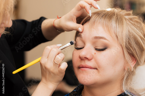 A woman's hand applies and shades the eye shadow with a makeup brush.