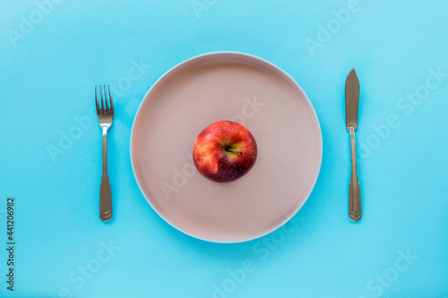 Red apple on a pink plate on blue background. Diet and weight loss concept. Top view, flat lay