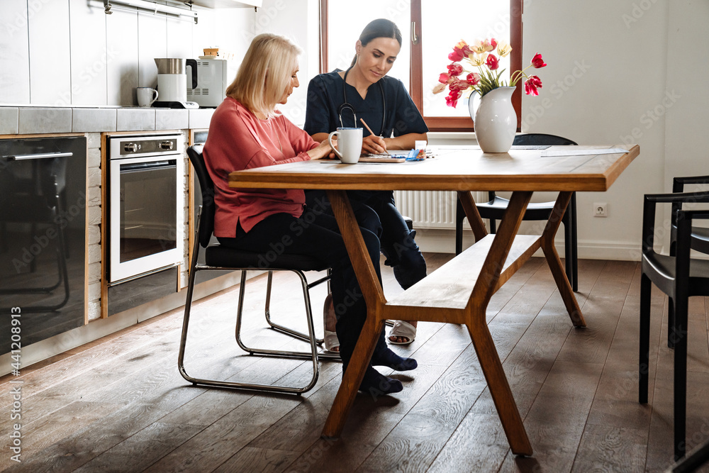 A side view of the concentrated doctor writing a prescription to her elderly patient A side view of the concentrated doctor writing a prescription to her elderly patient