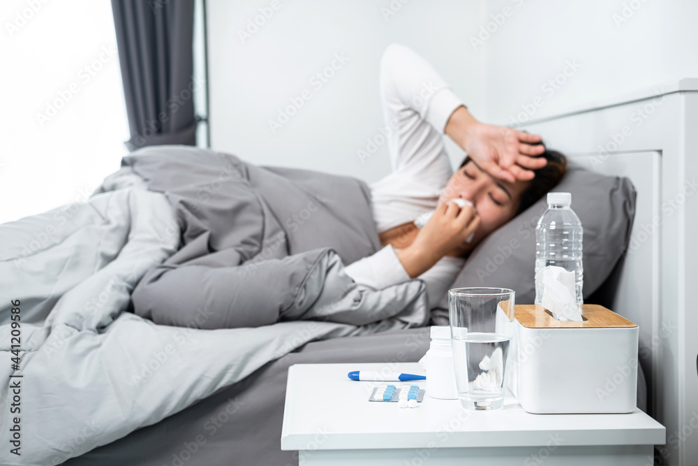 Asian woman feeling sick and sleeping in blanket on the bed while using tissue to cough, sneezing Asian woman feeling sick and sleeping in blanket on the bed while using tissue to cough, sneezing