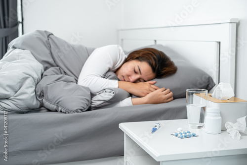 Asian woman feeling sick and sleeping in blanket on the bed after using thermometer to checking measure