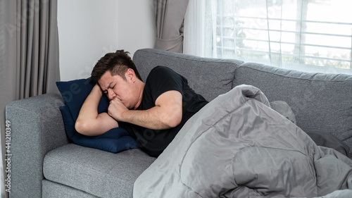 Bild auf Leinwand Asian man is lying with blanket on couch at home to rest when having high fever,