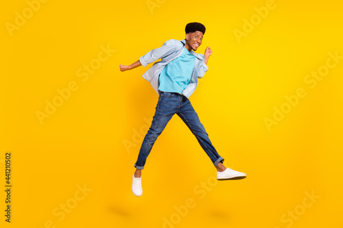 Photo of lucky funky dark skin man wear jeans shirt jumping high rising fists smiling isolated yellow color background © deagreez