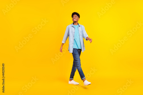 Photo of handsome attractive dark skin guy dressed denim shirt walking looking empty space isolated yellow color background