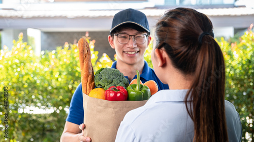 Asian delivery man in blue uniform holding grocery bag of food, fruit, vegetable give to woman customer