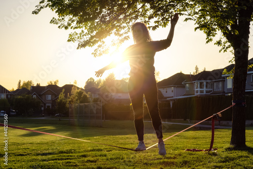 Obraz na płótnie Adventurous White Caucasian Adult Woman walking on a Slackline between trees in a neighborhood park