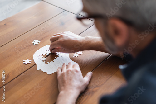 Blurred man with dementia folding jigsaw on table at home photo
