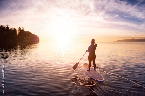 Adventurous girl on a paddle board is paddeling in the Pacific West Coast Ocean. Sunset Sky Art Render. Taken near Spanish Banks, Vancouver, British Columbia, Canada.