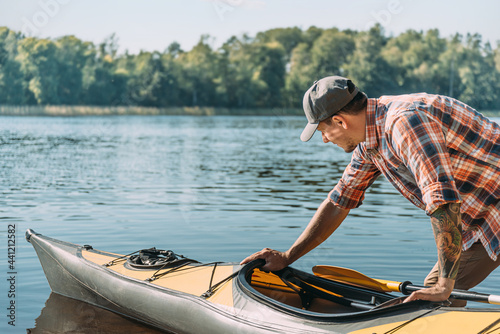 Young man with a tattoo in a cap and shirt launching a kayak. photo