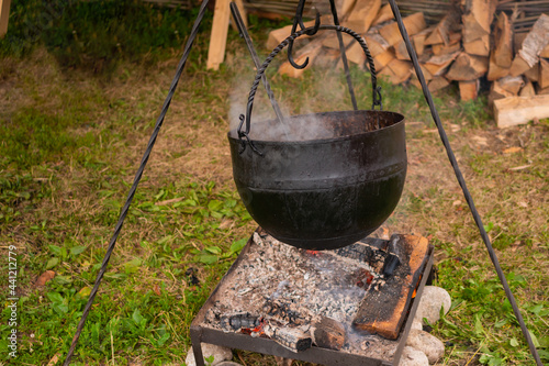 Preparing food in hanging black pot over open fire at historical festival - close up view. Outdoor cooking, hiking, tourism, travelling, camping concept
