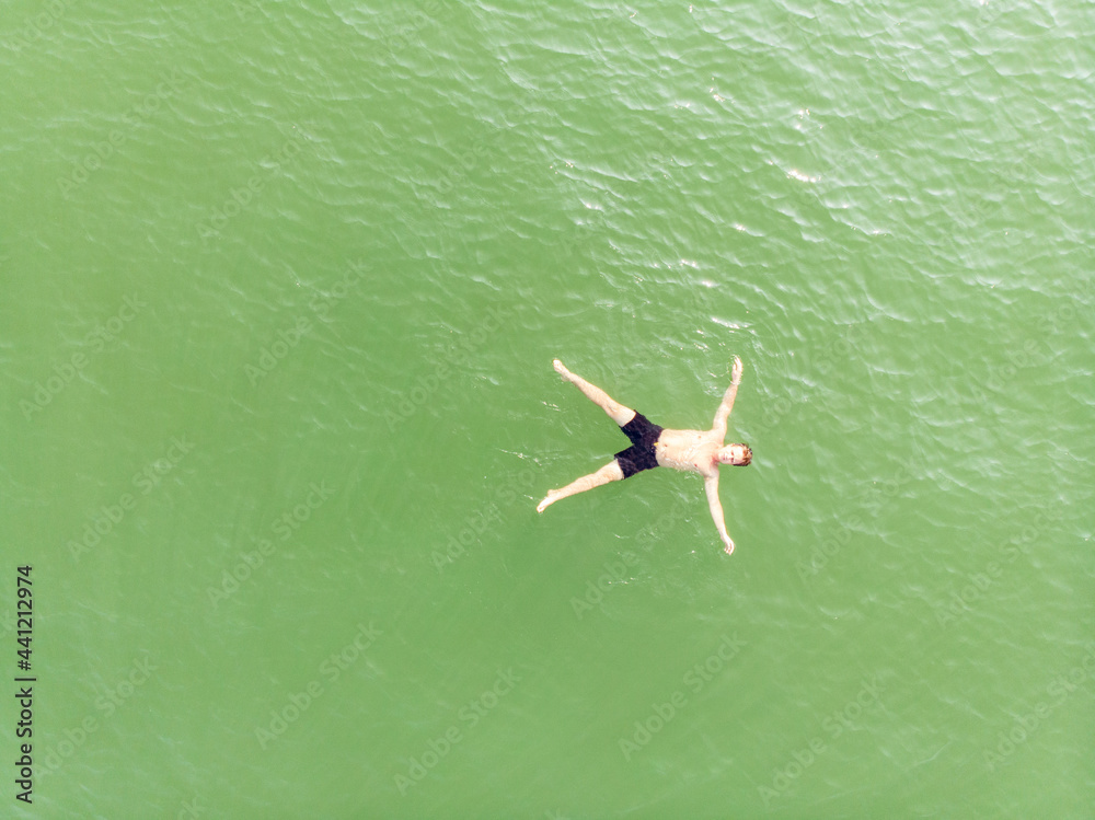 guy in shorts swims on his back in sea. Top view. Aerial shot.