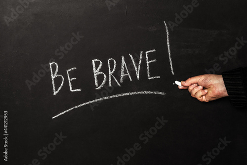 A man writes on a black board with white chalk the phrase Be brave! photo