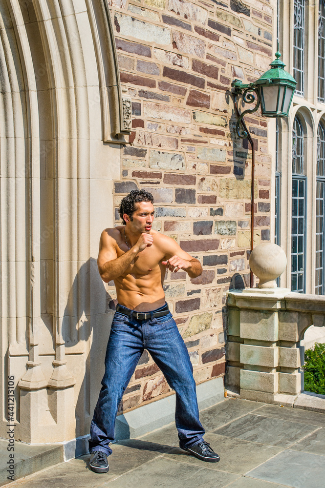 Dressing in jeans and leather sneakers and half naked, a handsome, muscular guy is waving arms and exercising to counterattack