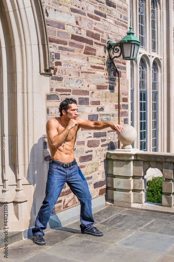 Dressing in jeans and leather sneakers and half naked, a handsome, muscular guy is waving arms and exercising to counterattack