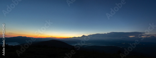 Panorama of the Carpathian mountains at sunset and the lights of the village in the haze, rest and travel in the mountains