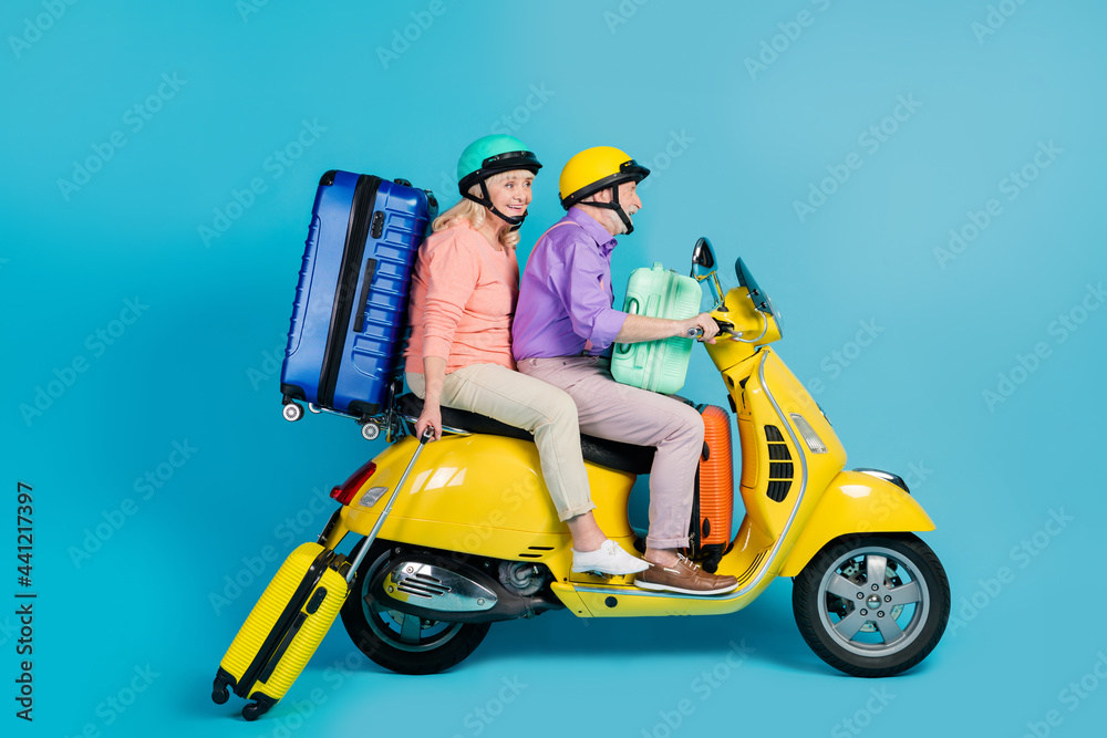 Photo of charming cute grandmother grandfather motorcyclist wear helmets holding luggage smiling isolated blue color background Photo of charming cute grandmother grandfather motorcyclist wear helmets holding luggage smiling isolated blue color background