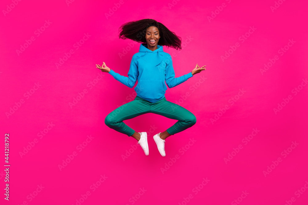 Photo of funny peaceful dark skin woman dressed blue sweatshirt smiling jumping high practicing yoga isolated pink color background