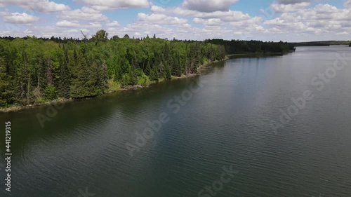 4K clip of drone circling to show beautiful, green, treed coastline next to blue rippling water at Lake Itasca, MN. Cloudy sky in background.