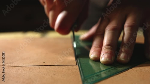 Leather craftsman making at work. Close up of his hands cutting leather using a small knife and a bracket