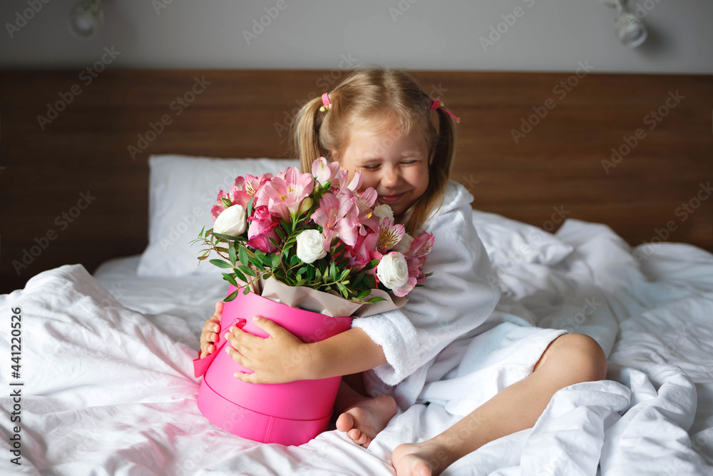 Little girl in a robe holds a box of flowers while sitting on the bed Little girl in a robe holds a box of flowers while sitting on the bed