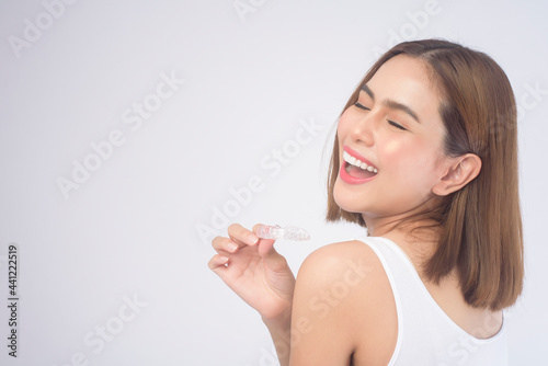 Young smiling woman holding invisalign braces over white background studio, dental healthcare and Orthodontic concept.
